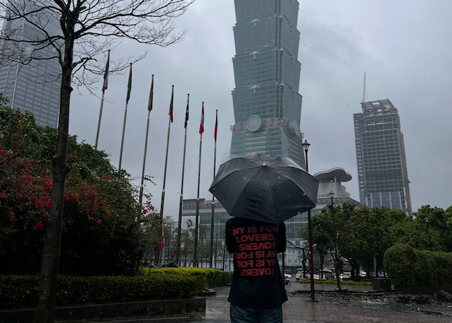 Naj holding an umbrella in the pouring rain near Taipei 101 building